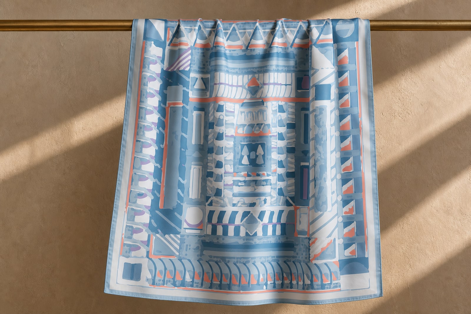 A printed silk scarf hanging from a brass rail against a warm plaster wall