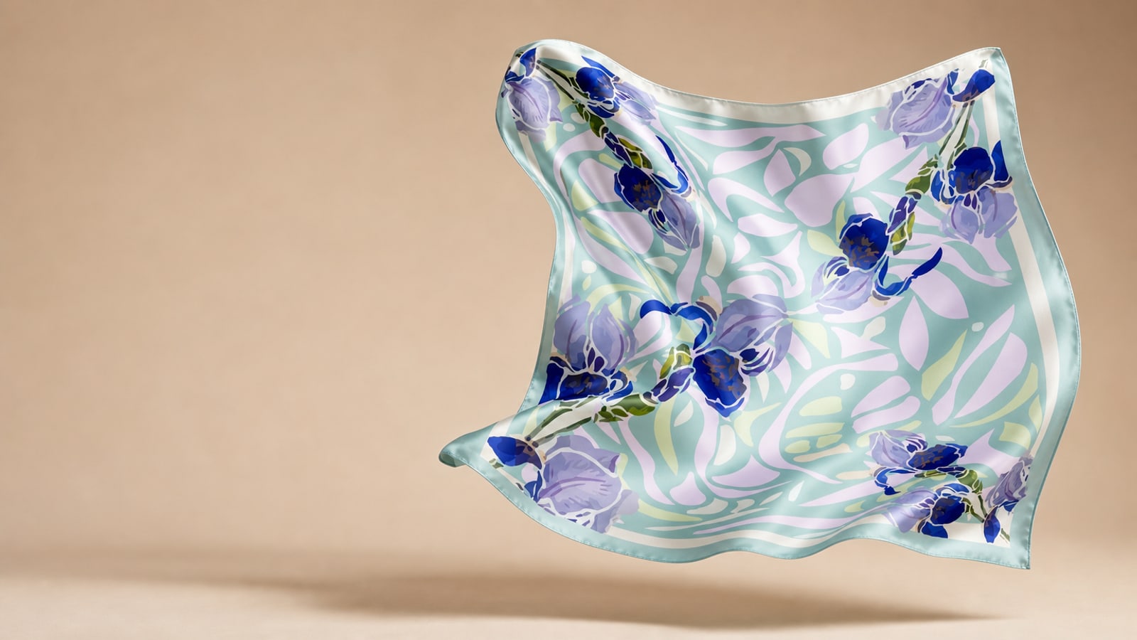 A printed silk scarf caught mid-air against a warm studio sweep